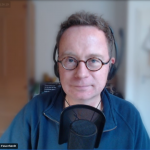 Der Publizist Alex Feuerherdt, ein Mann Ende 40 mit kurzen brauen Haaren und einer Brille, spricht in ein Mikrofon. Er trägt ein Headset